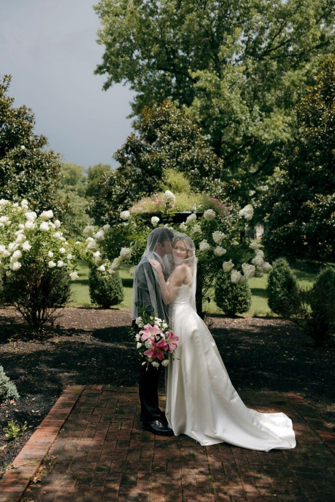 A groom giving his bride a kiss on the cheek in the middle of a beautiful garden landscape at My Old Kentucky Home in Bardstown, Kentucky.