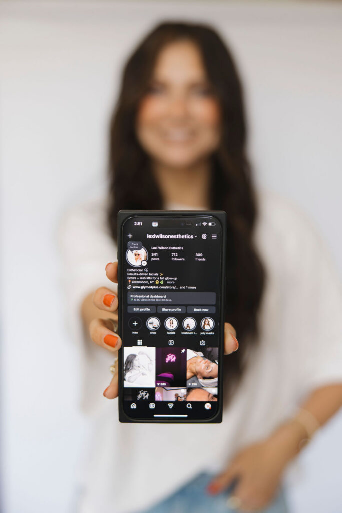 Louisville branding photographer | Lexi Wilson esthetics holding her phone up to show her instagram account.