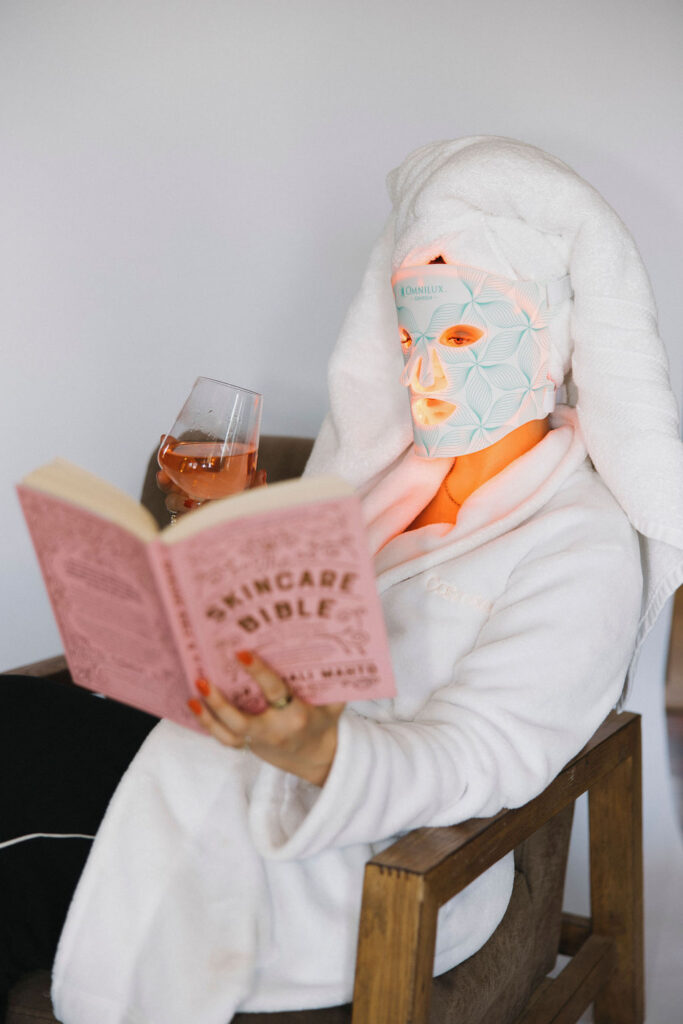 Louisville branding photographer | an esthetician wearing a red light mask and reading a book entitled the 'skincare bible'.