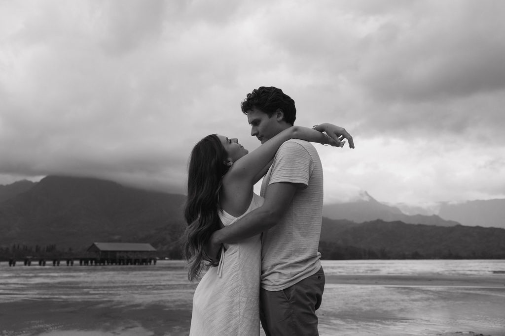 Engaged couple framed by Kauai’s green mountains and cloudy skies