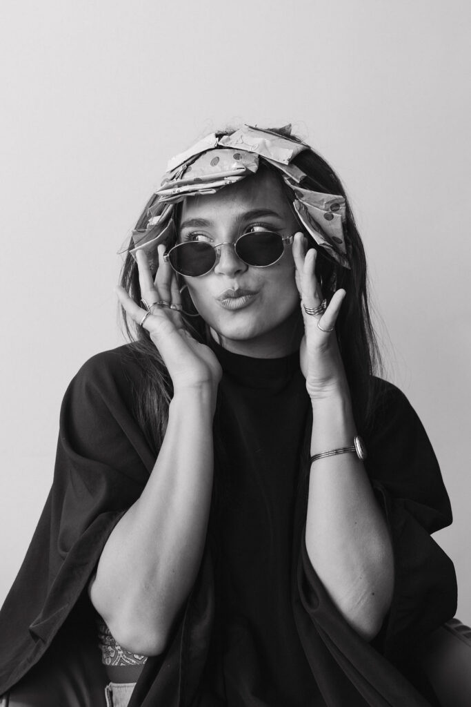 Black and white photo of a hair client wearing foils, sunglasses while making a cute face.