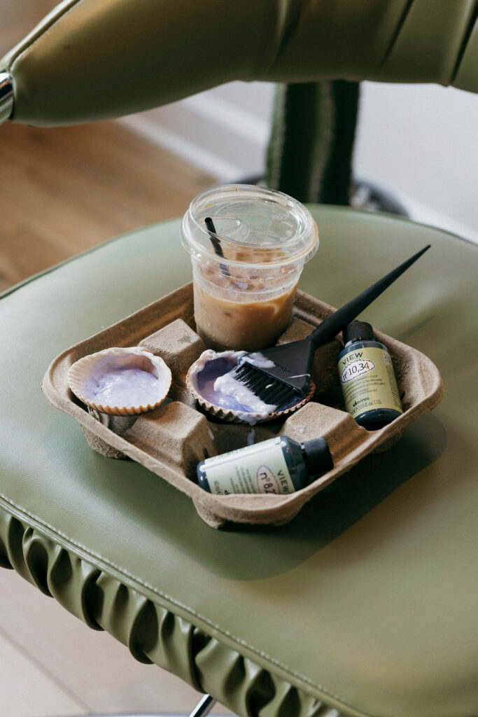 Coffee, hair products and styling tools arranged on a vintage green salon chair.