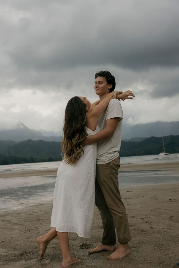 Couple embracing during a moody engagement session on Hanalei Beach in Kauai