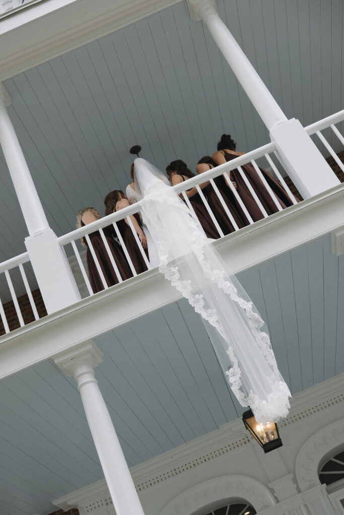 The bride's veil hanging over the railing as she is taking photos with her bridesmaids.
