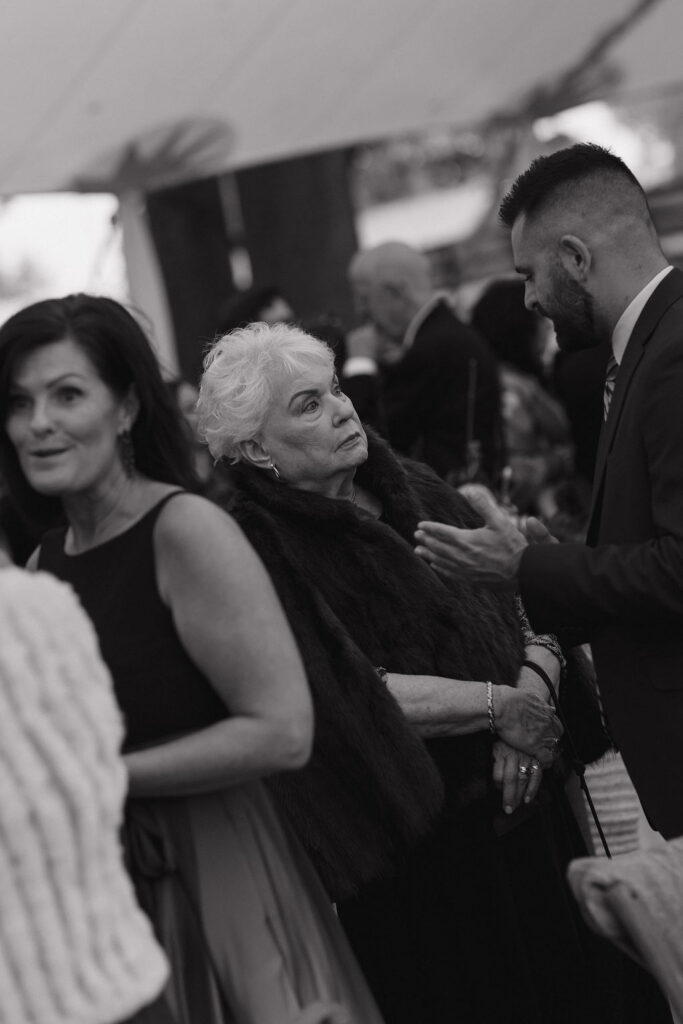 Black and white photo of a guest at cocktail hour in a stylish fur coat at a black tie wedding at Hermitage Farm in Kentucky.