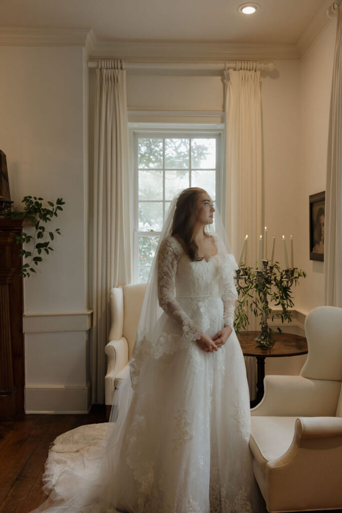 Bride with a gorgeous lace gown and a lace veil draping her as she looks out of the window.