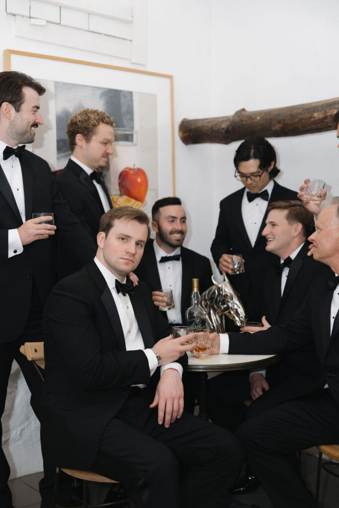 Groom and groomsmen holding drinks during indoor wedding portraits.