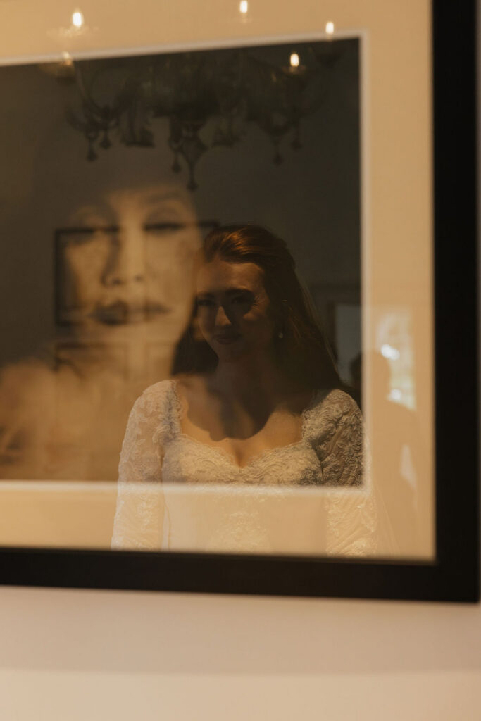 Bride’s reflection appearing in the glass of framed artwork