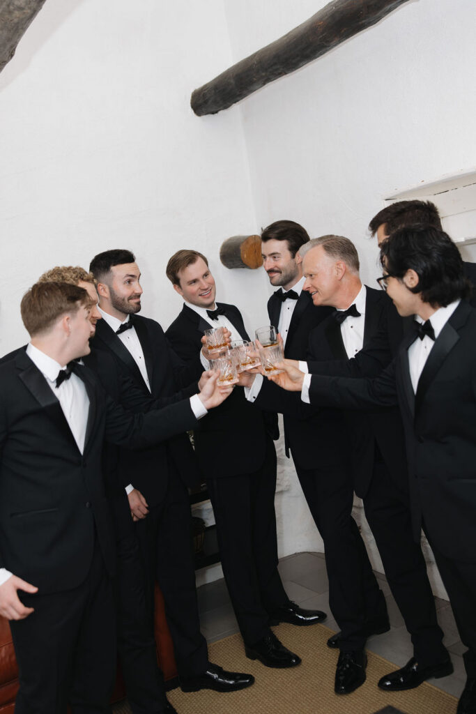 Groom and groomsmen holding drinks during indoor wedding portraits.