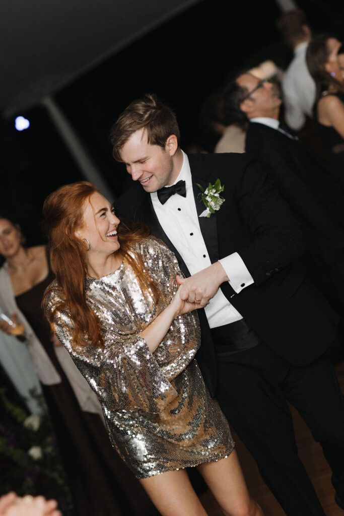 Bride in a sparkling short dress dancing beside the groom at their wedding reception.