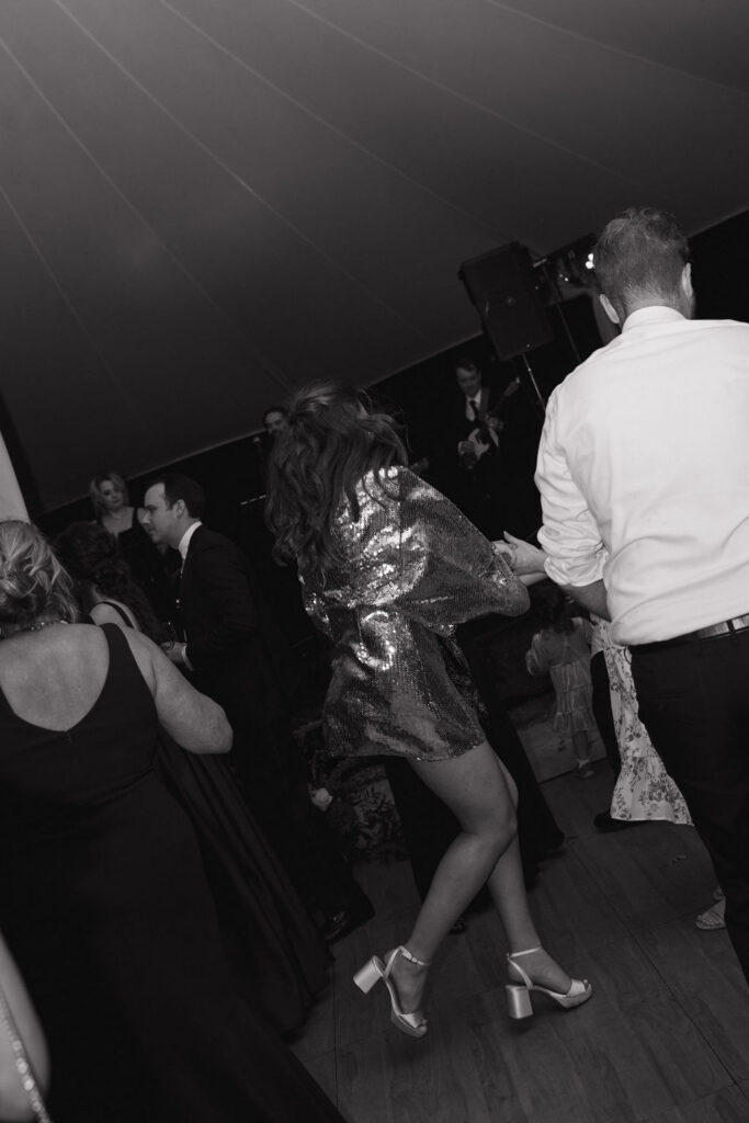Bride celebrating on the dance floor in a sparkling reception dress in black and white photo.
